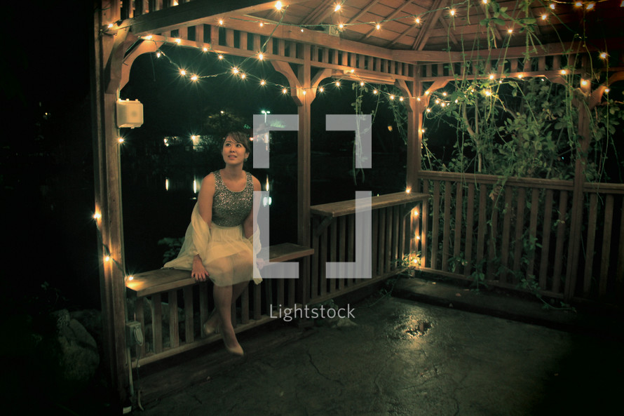 Woman sitting in a lighted gazebo at night.