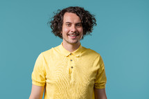 Friendly 30s white man smiling portrait. Positive curly guy in yellow polo on blue studio. High quality photo