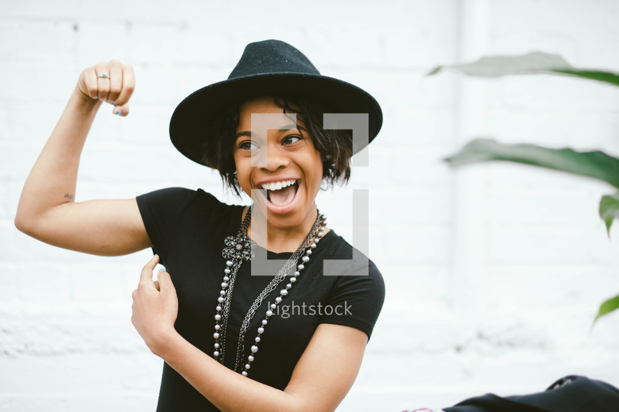 An African American woman in a black hat flexing her muscle 