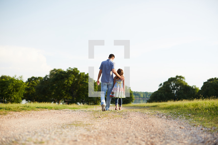 a father and daughter walking down a dirt road talking 