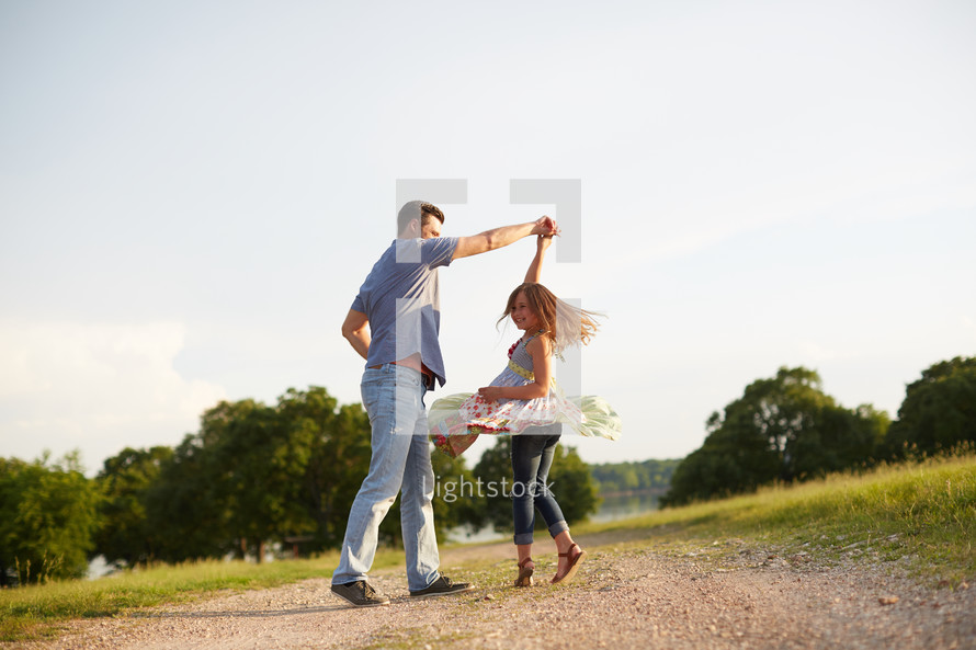 a father spinning his daughter on a dirt road 