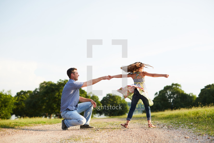 a father spinning his daughter on a dirt road 