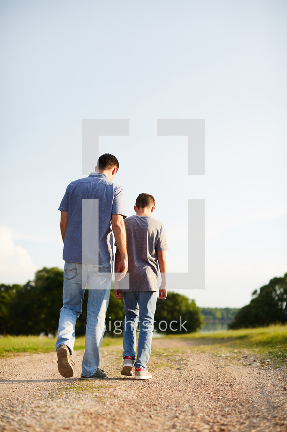 a father and son walking down a dirt road talking 