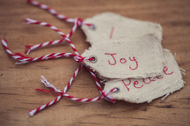 A stack of Christmas gift tags, the top one reading "Joy" on a wood grain background.