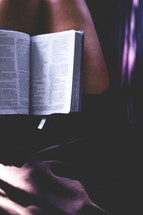 A woman sits with an open Bible in her lap.