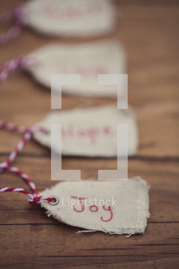 Christmas gift tags lined up on a wooden table, the first one reading, "Joy."