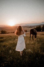 Woman in white dress walking by horse at sunset