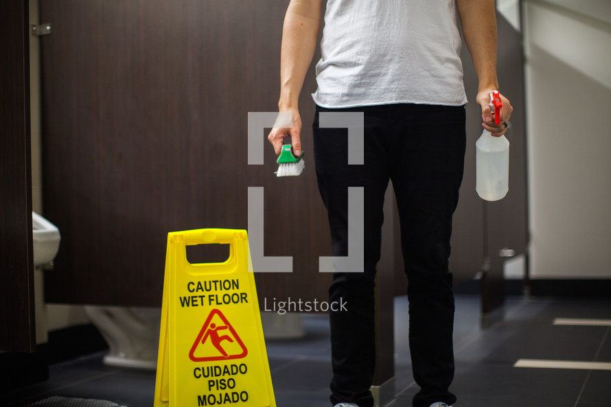 a man with a spray bottle and brush in a public restroom 