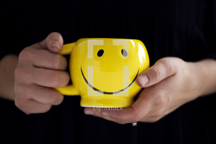 woman holding a smiley face coffee mug.