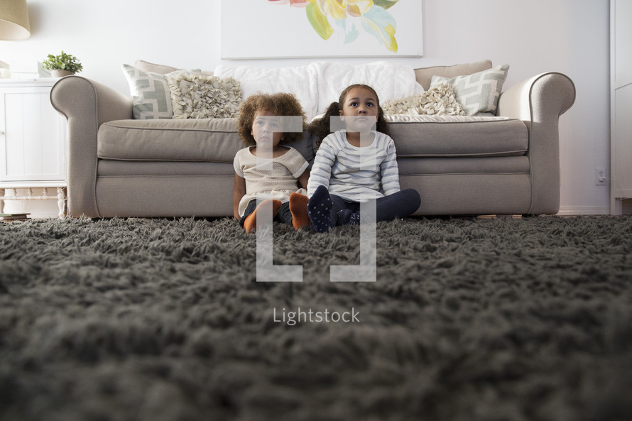 sisters sitting on a rug in a living room 