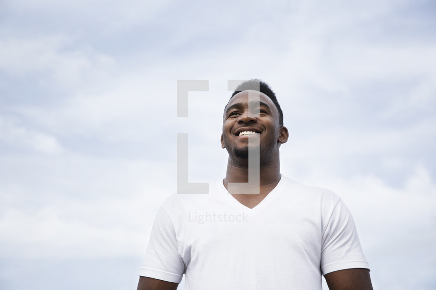 A smiling man against a cloudy white sky.