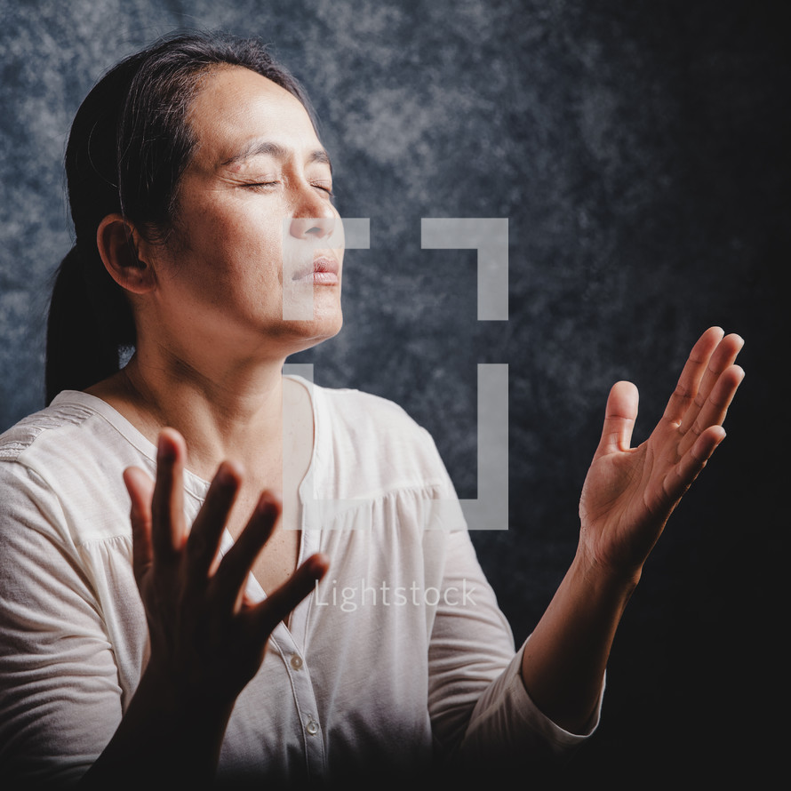 Asian woman praying with raised hands.