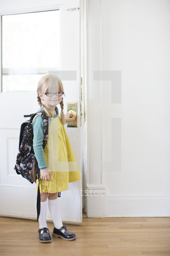 girl child with a book bag opening a door - first day of school 