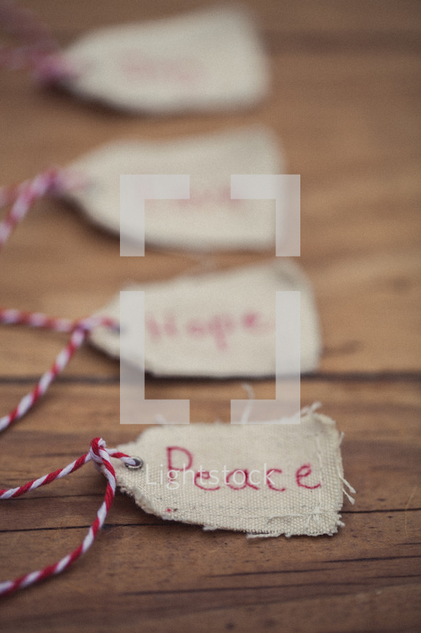 Christmas gift tags lined up on a wood grain background, with one reading "Peace" in the front.