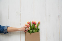 a woman reaching for a tulip in a brown paper bag 