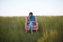 a woman sitting in a field reading a Bible 