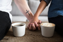 Two people holding hands between two cups of coffee.