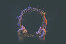 wo hands hold up crown of thorns