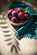 Plums in a bowl with green napkin and leaf shadow
