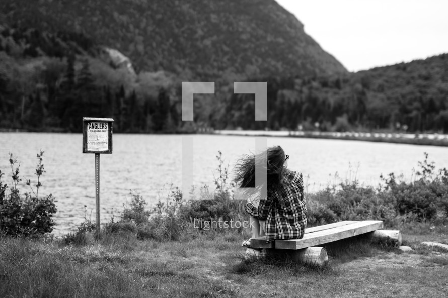 anglers sign near a river and a woman sitting on a bench