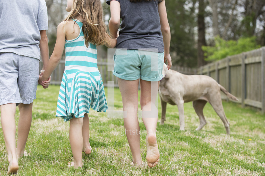 family walking holding hands in the back yard and a family dog 