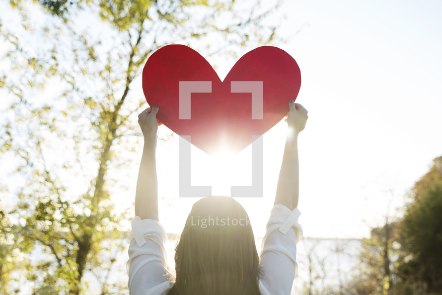 woman holding up a paper heart outdoors 