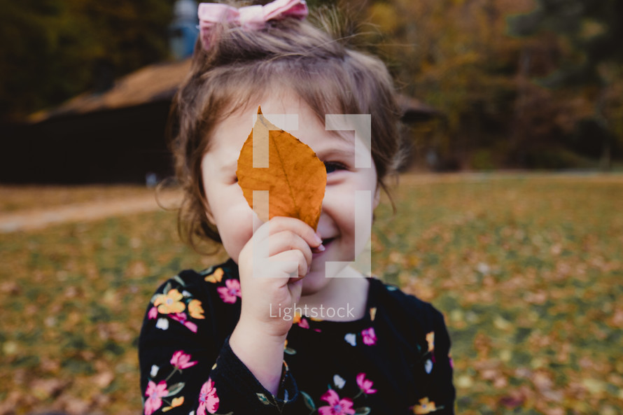 toddler holding a fall leaf in front of her face 