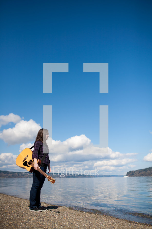 woman holding a guitar in front of a lake