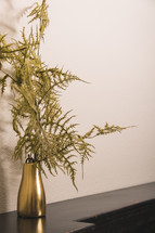 greenery in a gold vase on a mantle 