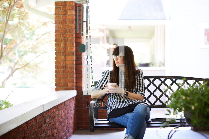 a woman sitting on a porch swing with a cup of coffee 