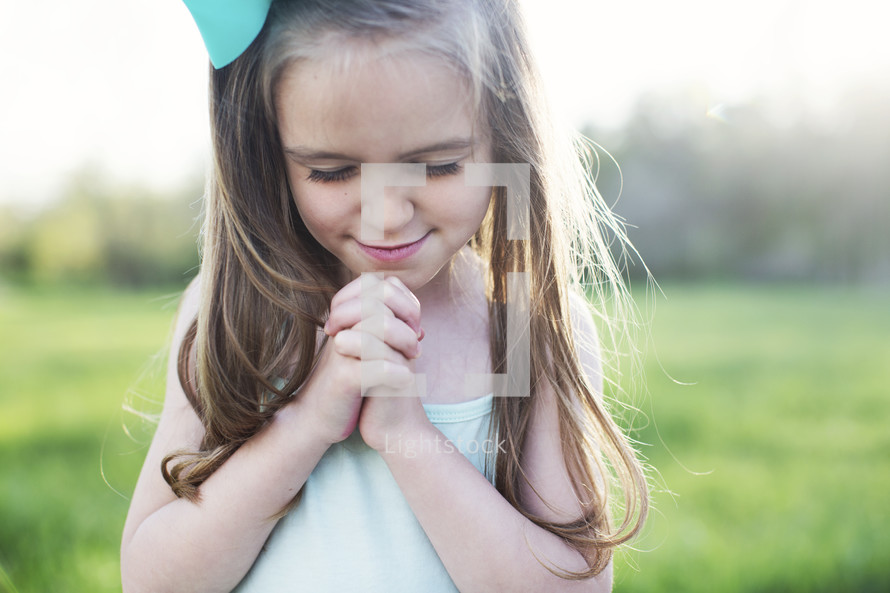 a little girl praying outdoors 