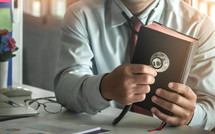 Medical professional holding the bible with stethoscope on desk.