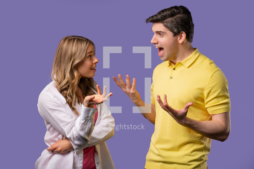 Young couple emotionally quarreling on violet background. Concept of conflict, problems in relationships. White american woman and man. High quality 