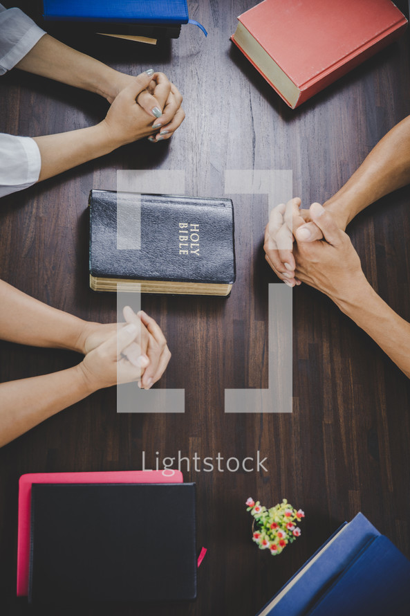 Group of people praying together around a table with Bibles