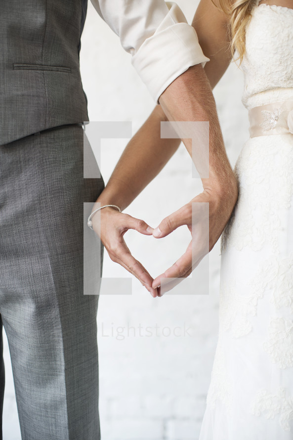 bride and groom making a heart shape with their hands 