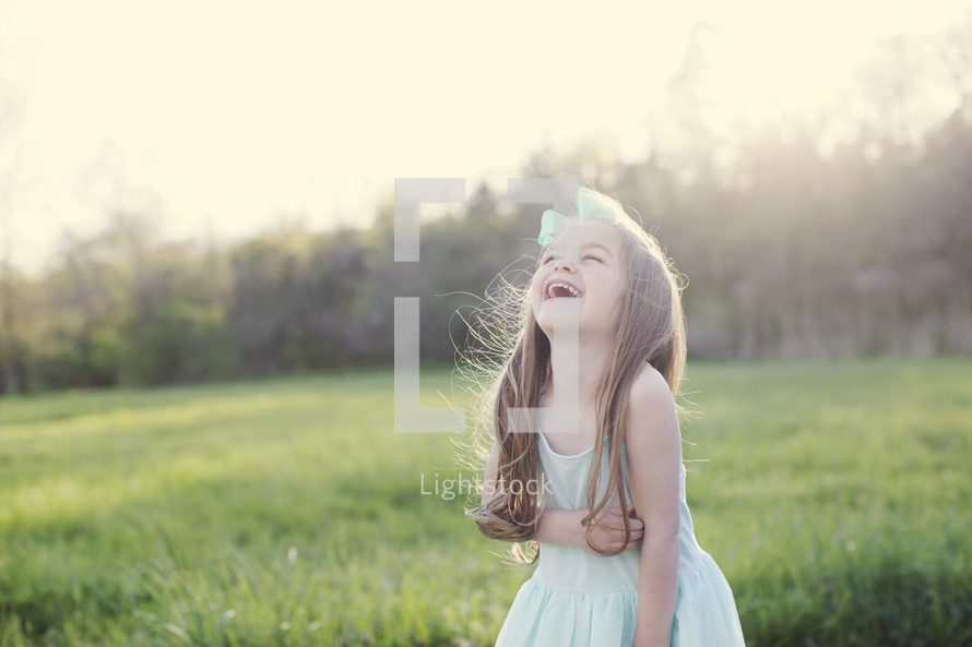 a little girl standing in a field of green grass laughing