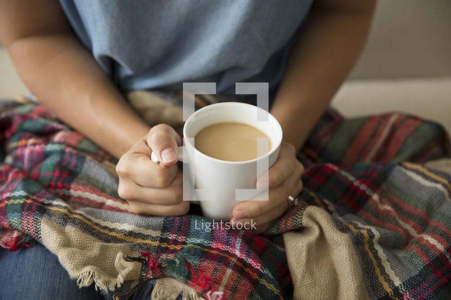 a woman with a plaid blanket in her lap holding a mug of coffee 