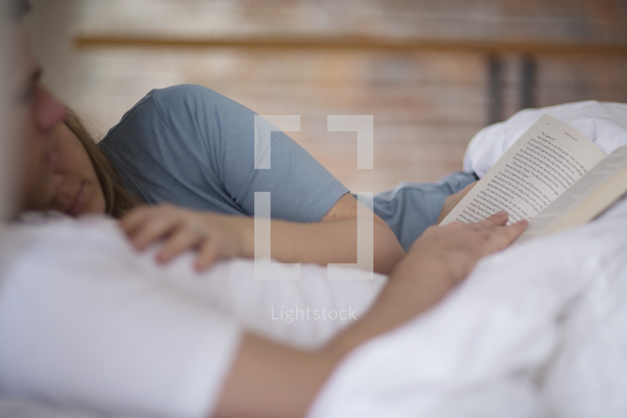 a couple lying in bed snuggling and reading a Bible 