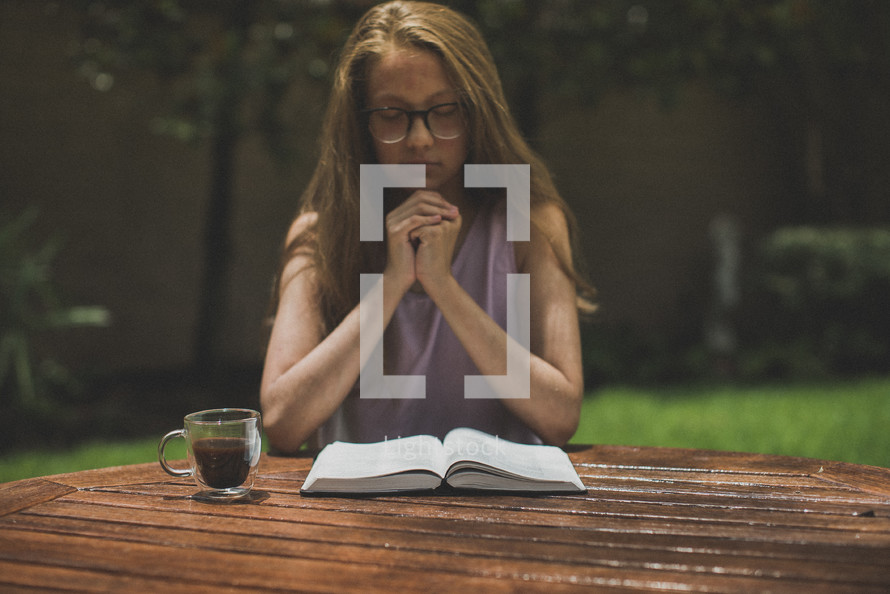 a young woman reading a Bible in her backyard and praying 