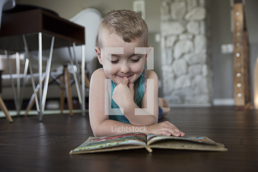 a toddler boy reading a book on the floor 