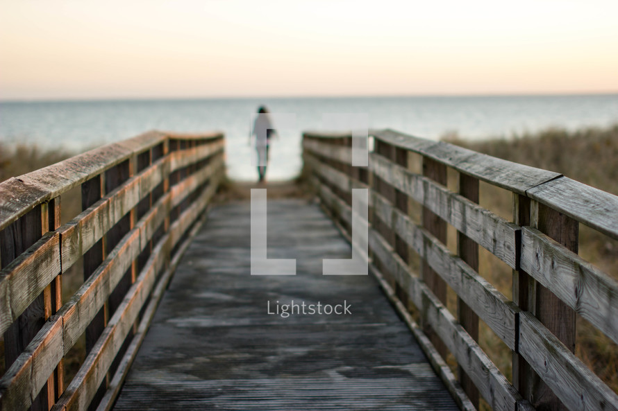 Woman at the end of a long pier leading into the ocean.