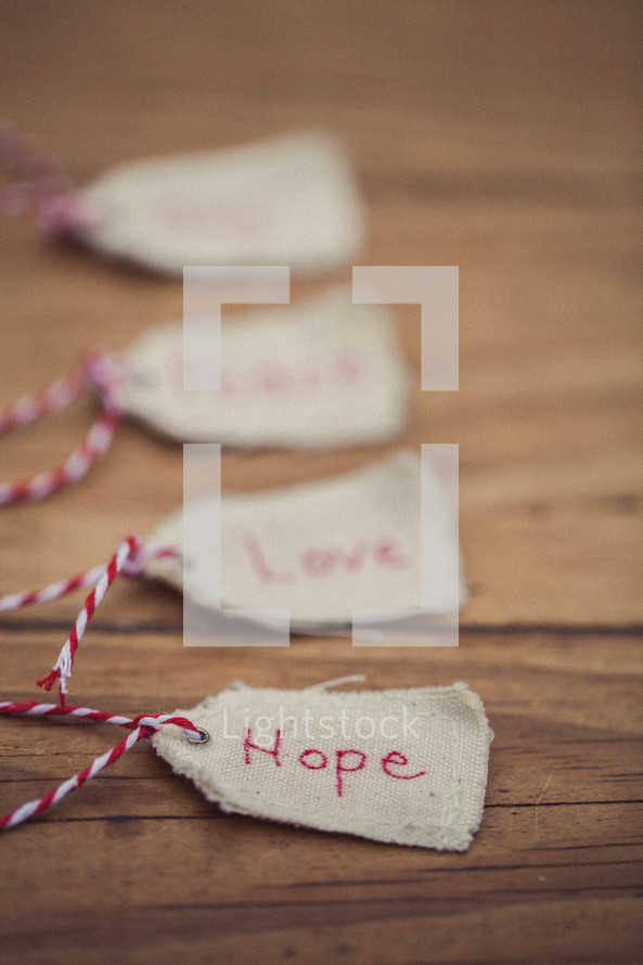 Christmas gift tags lined up on a wood grain background, with the word "Hope" on the first one in line.
