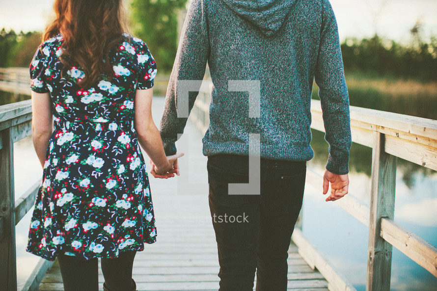 couple walking holding hands across a bridge 