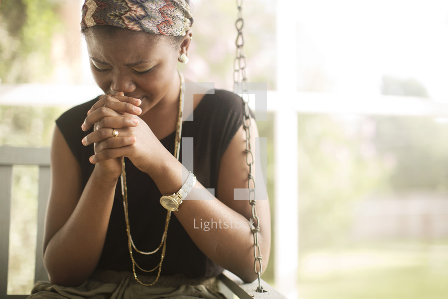 Woman sitting outside on a porch swing praying.