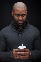 a man with his head bowed holding a candle 