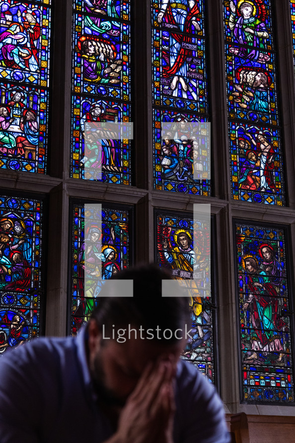 man praying in front of a stained glass window 
