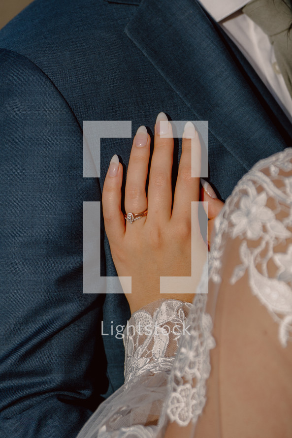 Close up of a bride resting her hand on husband's chest.