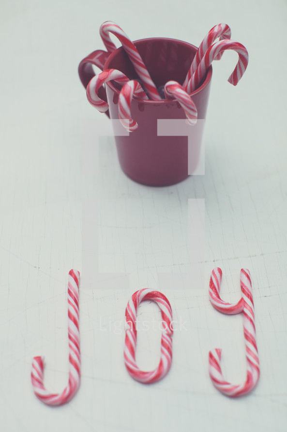 Candy canes in a red cup and spelling "joy".