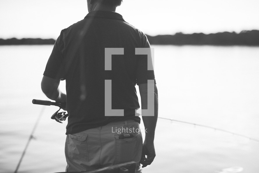 a man holding a fishing pole at a lake 