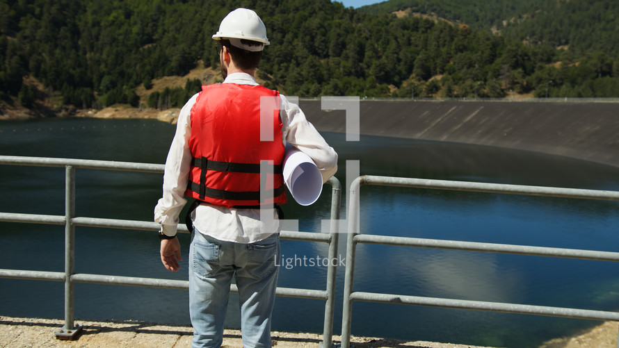 Engineer with white helmet holds a project of the new dam